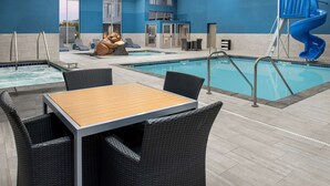 An indoor swimming pool area with a blue slide, lounge chairs, and a table with chairs.