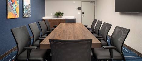A conference room with a long wooden table, black mesh chairs, and two abstract paintings on the wall.