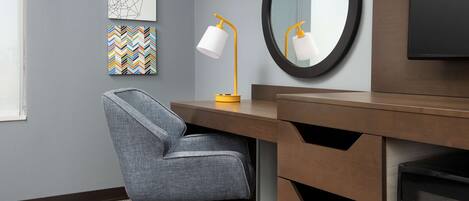 A modern office chair, a desk with a mirror, and a wall-mounted lamp.
