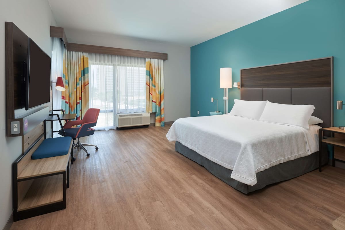 A hotel room with a large bed, a desk with a chair, a TV, and a window with curtains.