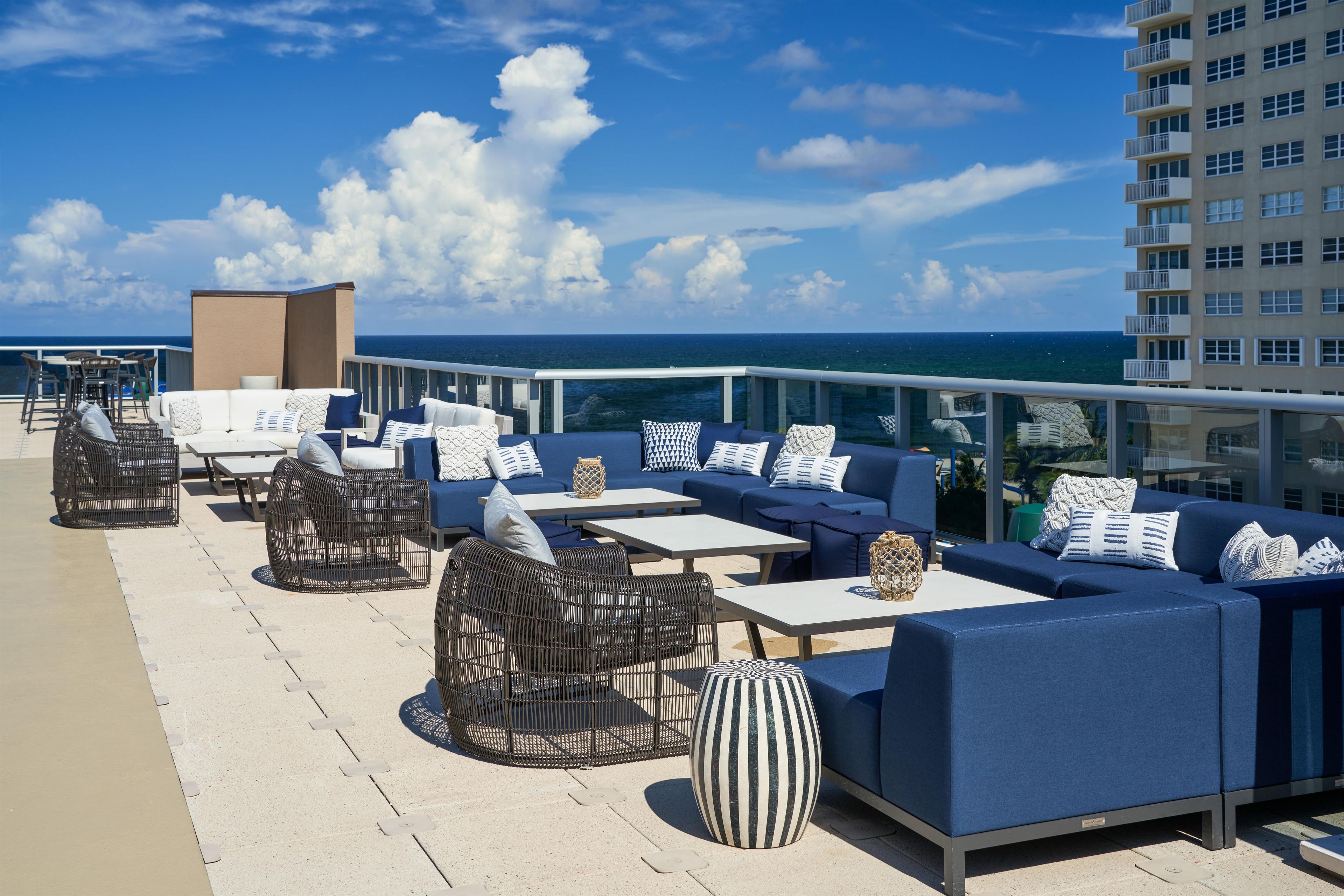 A rooftop bar with outdoor seating, including sofas and chairs, overlooking the ocean.