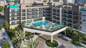 Un hotel con piscina en la azotea, varios balcones y un patio ajardinado.