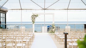 Montaje para una ceremonia de boda al aire libre con un pasillo blanco, decoración floral y vista al océano.