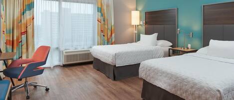 A hotel room with two beds, a desk, a chair, a lamp, and a window with curtains.