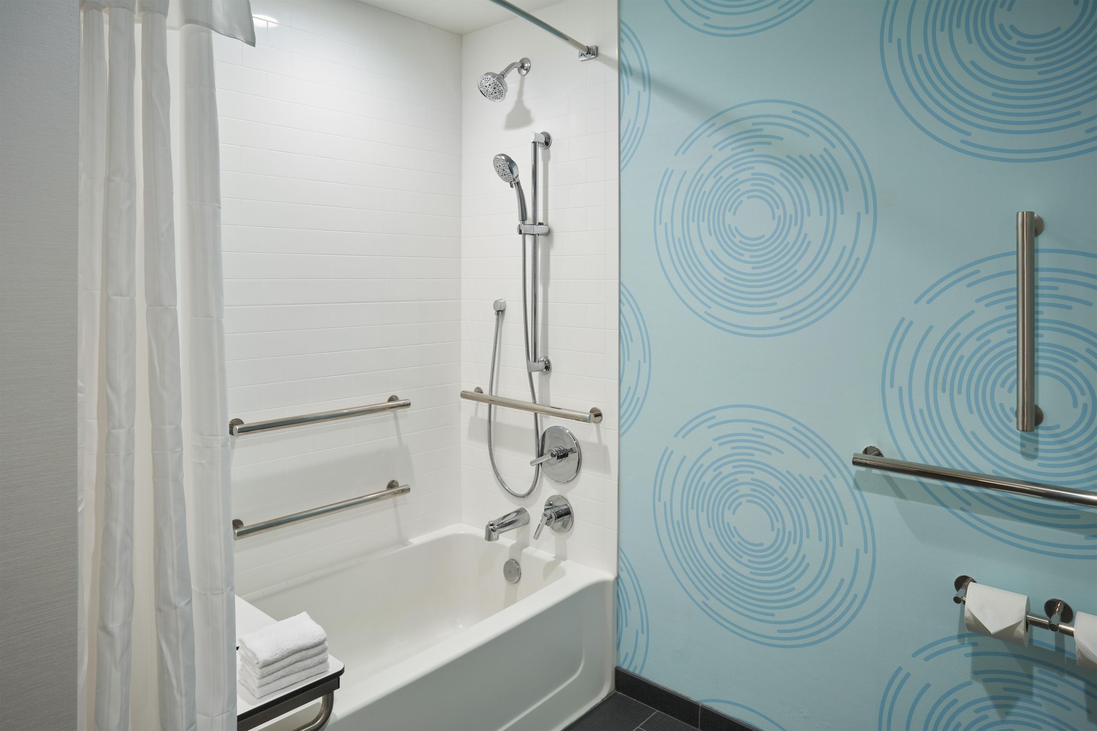 A modern bathroom with a white bathtub, a shower with a handheld showerhead, and a towel rack.