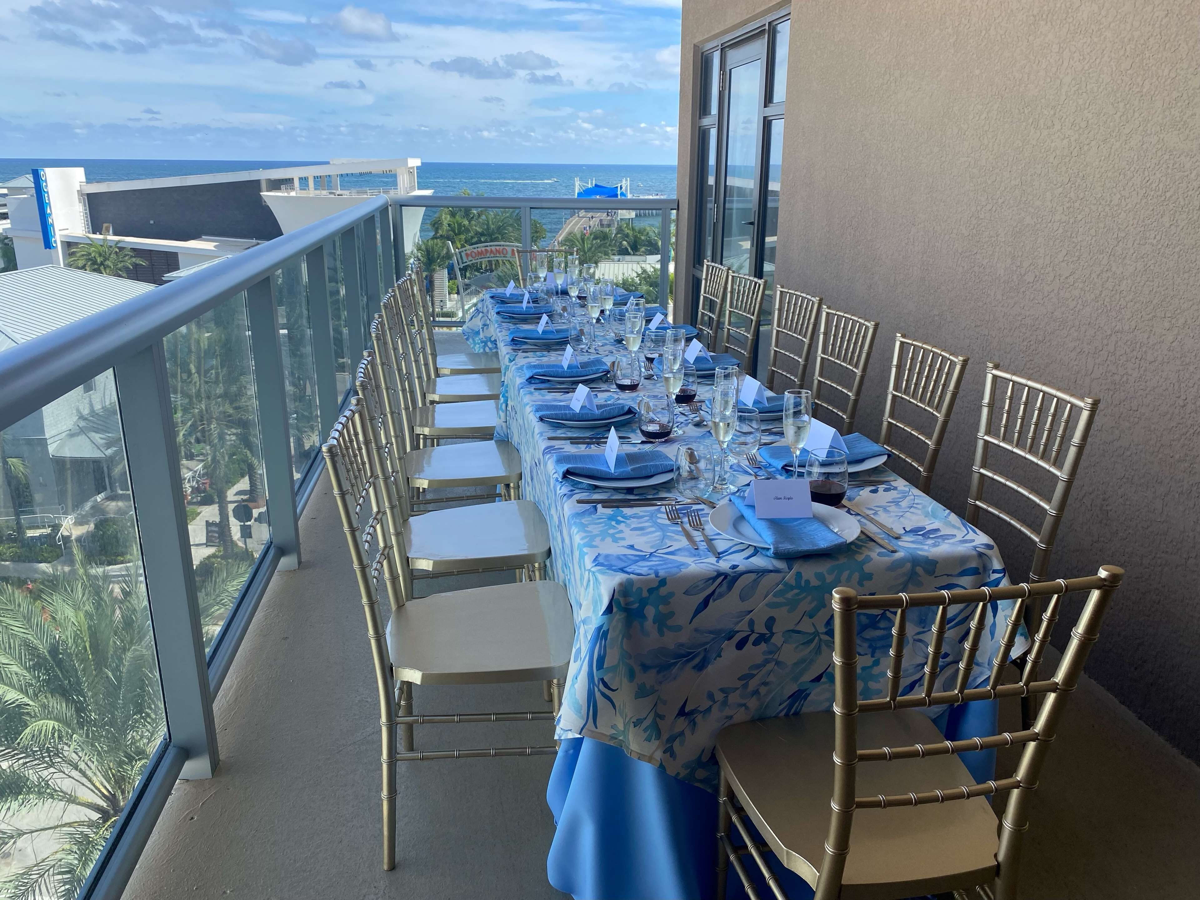 A balcony with a long table set for dining, overlooking the ocean.
