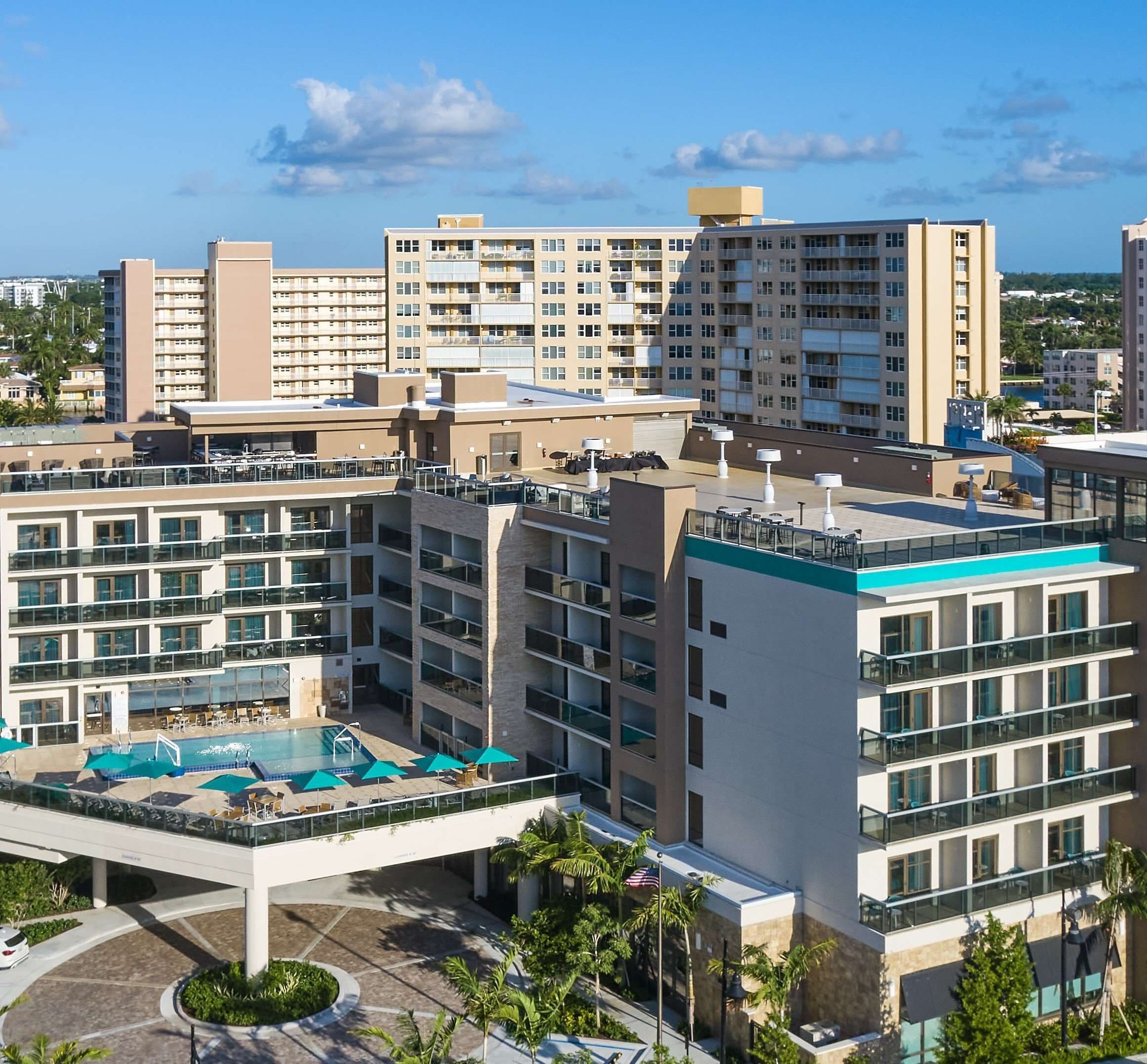A multi-story hotel with a rooftop pool area, outdoor seating, and a view of surrounding buildings.