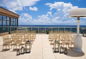 An outdoor seating area with bamboo chairs and tables, arranged for an event, overlooking a body of water and a clear sky. - Tru By Hilton Pompano Beach Pier (Pompano Beach)