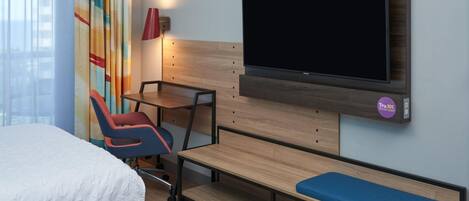 Une chambre d’hôtel équipée d’un lit, d’un bureau, d’une chaise, d’un banc et d’un téléviseur fixé au mur.