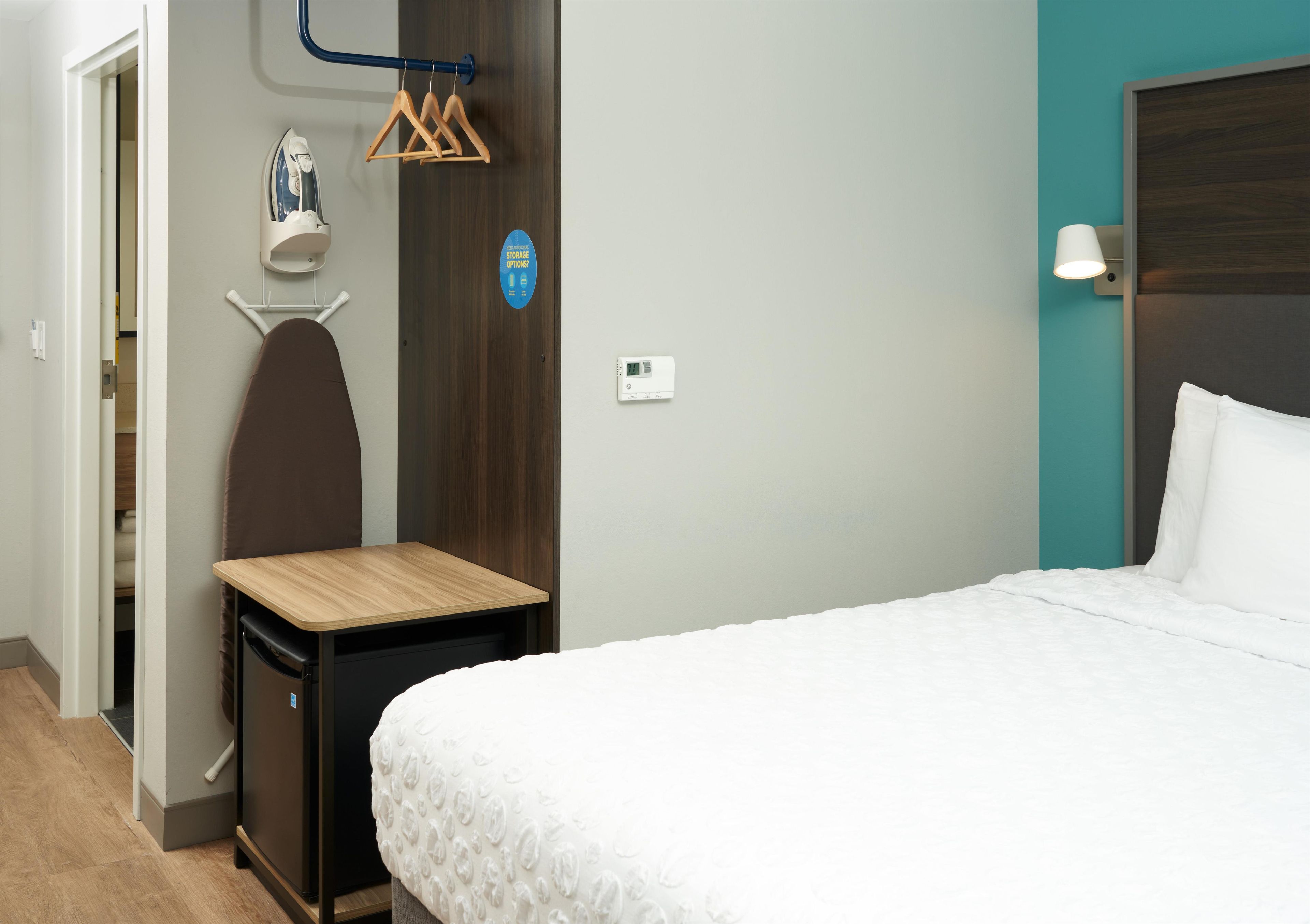 Habitación de hotel con una cama, una mesita, un armario, una tabla de planchar y un calentador de pared.