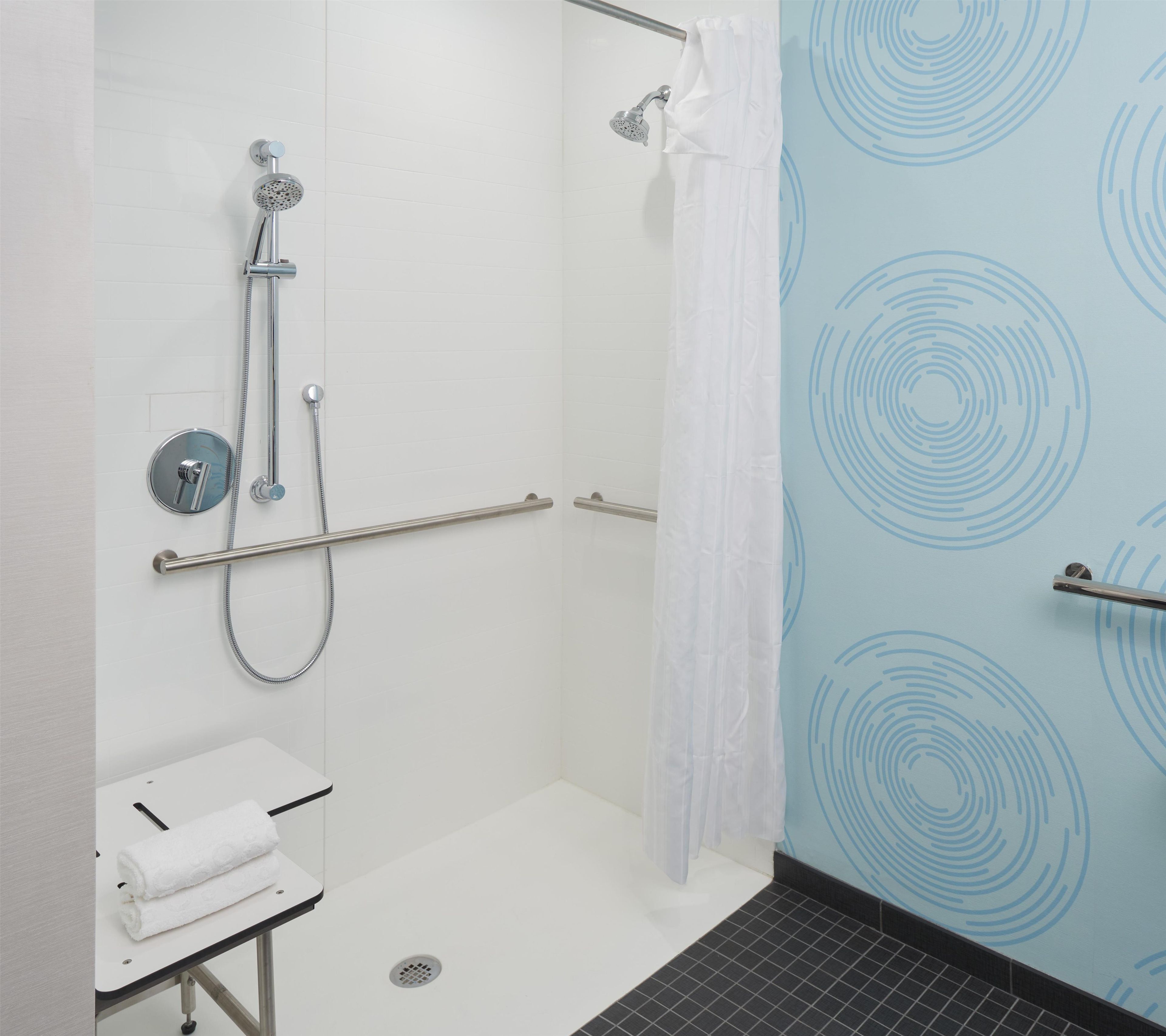 A modern bathroom with a walk-in shower, grab bars, a towel rack, and a toilet.
