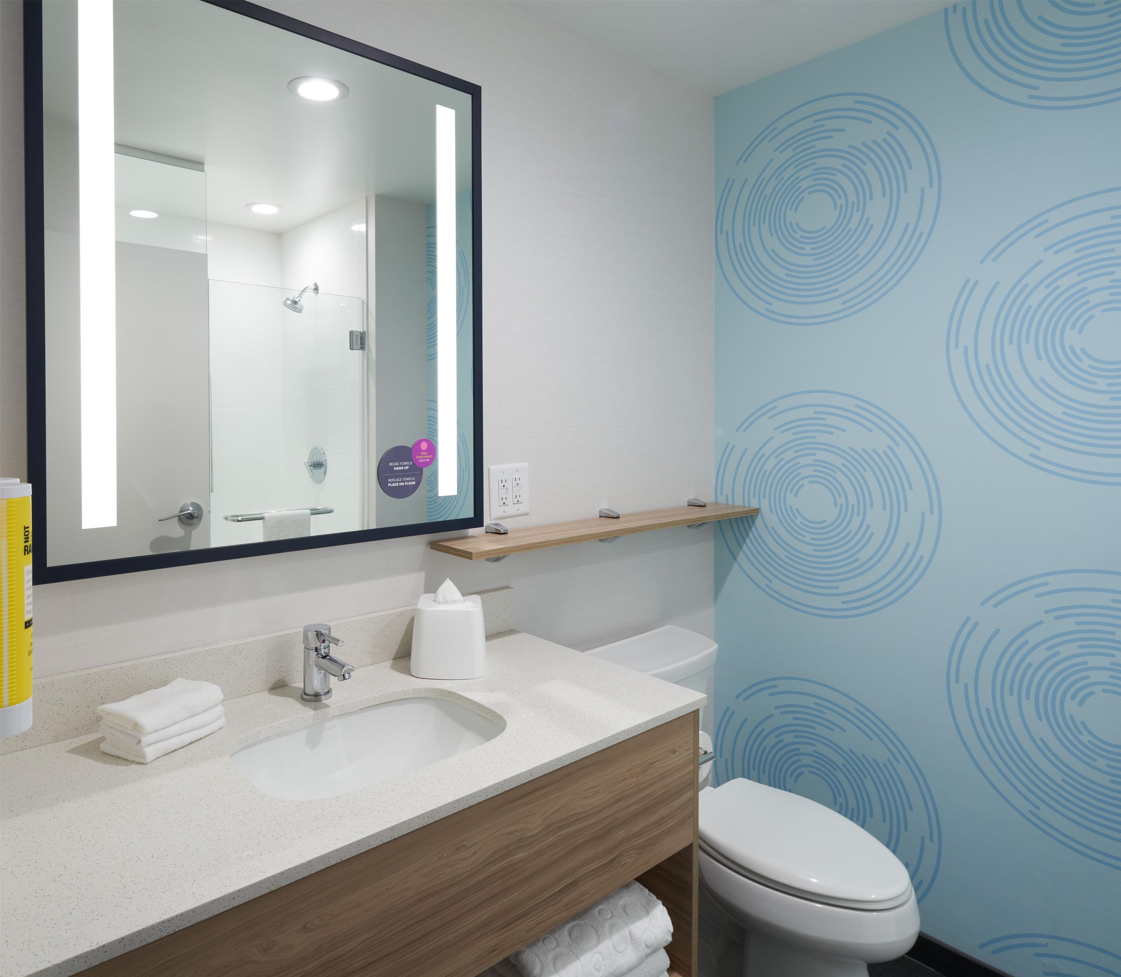 A modern bathroom with a large mirror, a sink, a toilet, and a towel dispenser.