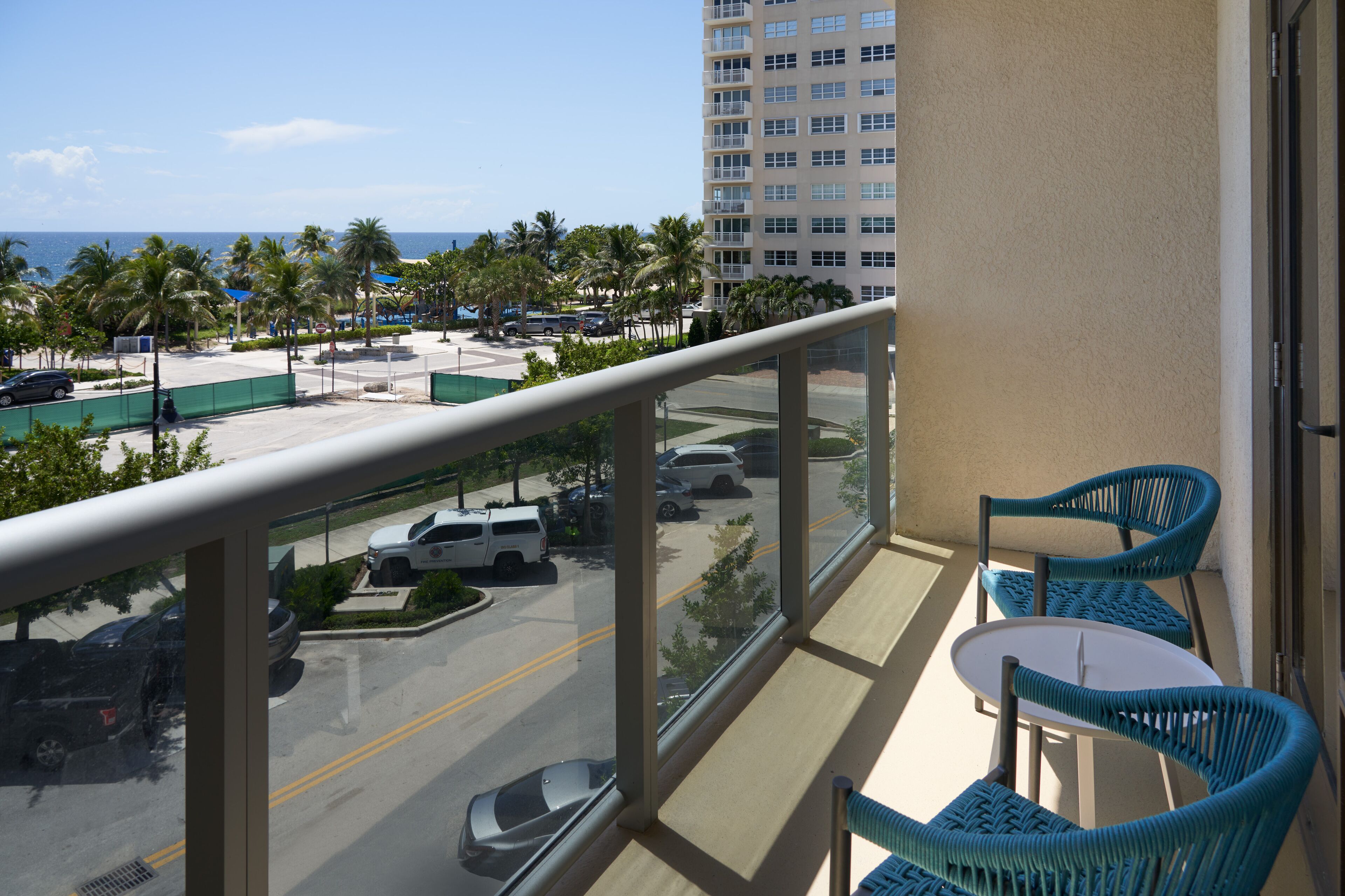 A balcony with a view of a parking lot, palm trees, and a tall building.