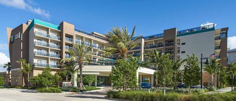 A multi-story hotel with balconies, palm trees, and a clear blue sky.