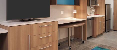 A modern kitchen with wooden cabinets, a microwave, a refrigerator, and a flat-screen TV.
