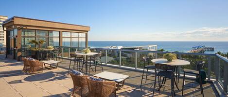 A terrace with wicker furniture, a glass balustrade, and a view of the sea.