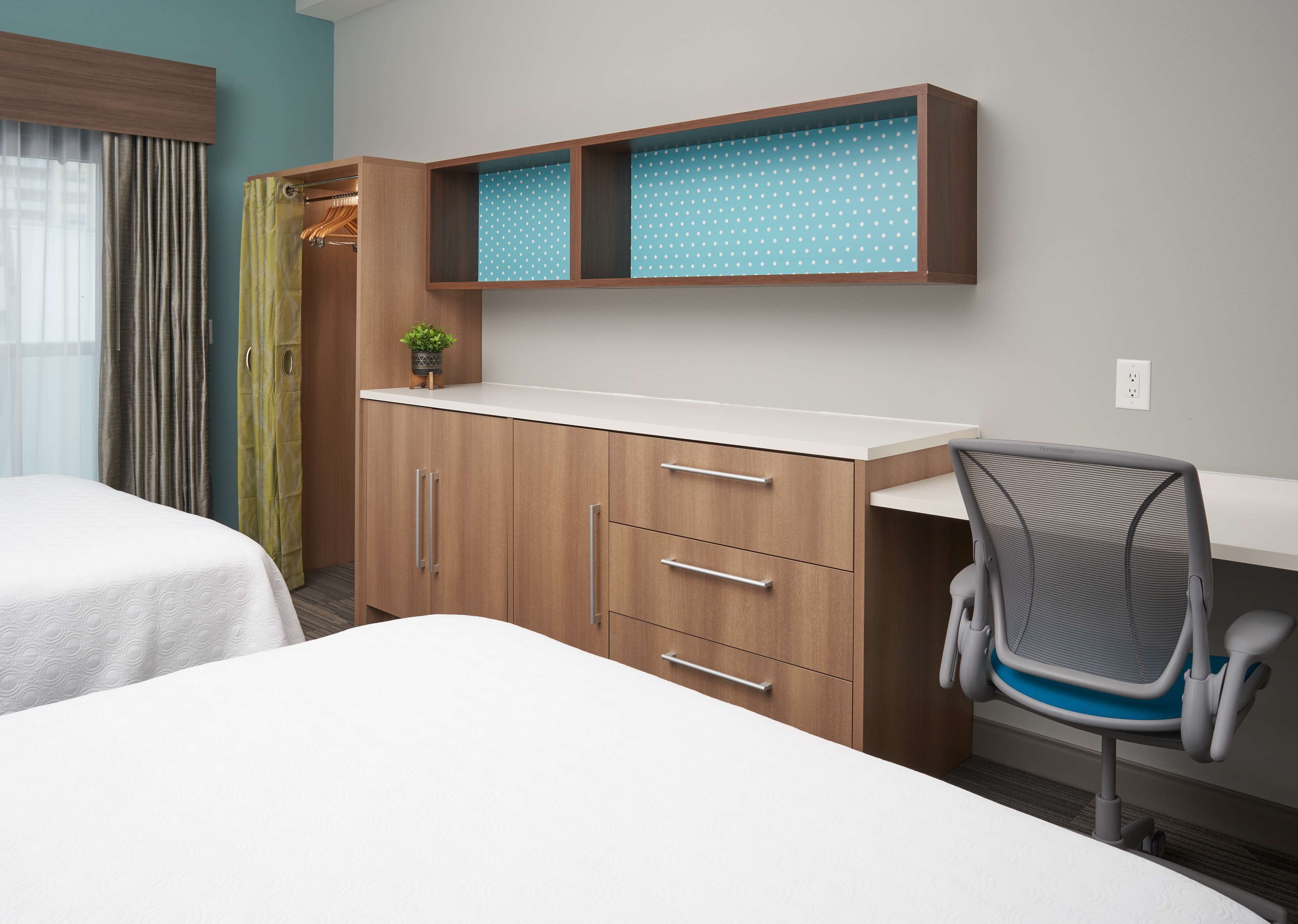 Een hotelkamer met een bed, een bureau met stoel, een kledingkast en een kleine plant op het bureau.