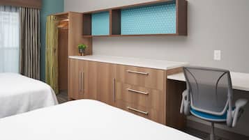 Een hotelkamer met een bed, een bureau met stoel, een kledingkast en een kleine plant op het bureau.