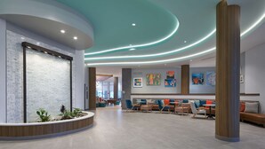 Eine moderne Lobby mit einer gebogenen Rezeption, einer Sitzecke mit Sofas und Tischen sowie Kunstwerken an den Wänden.