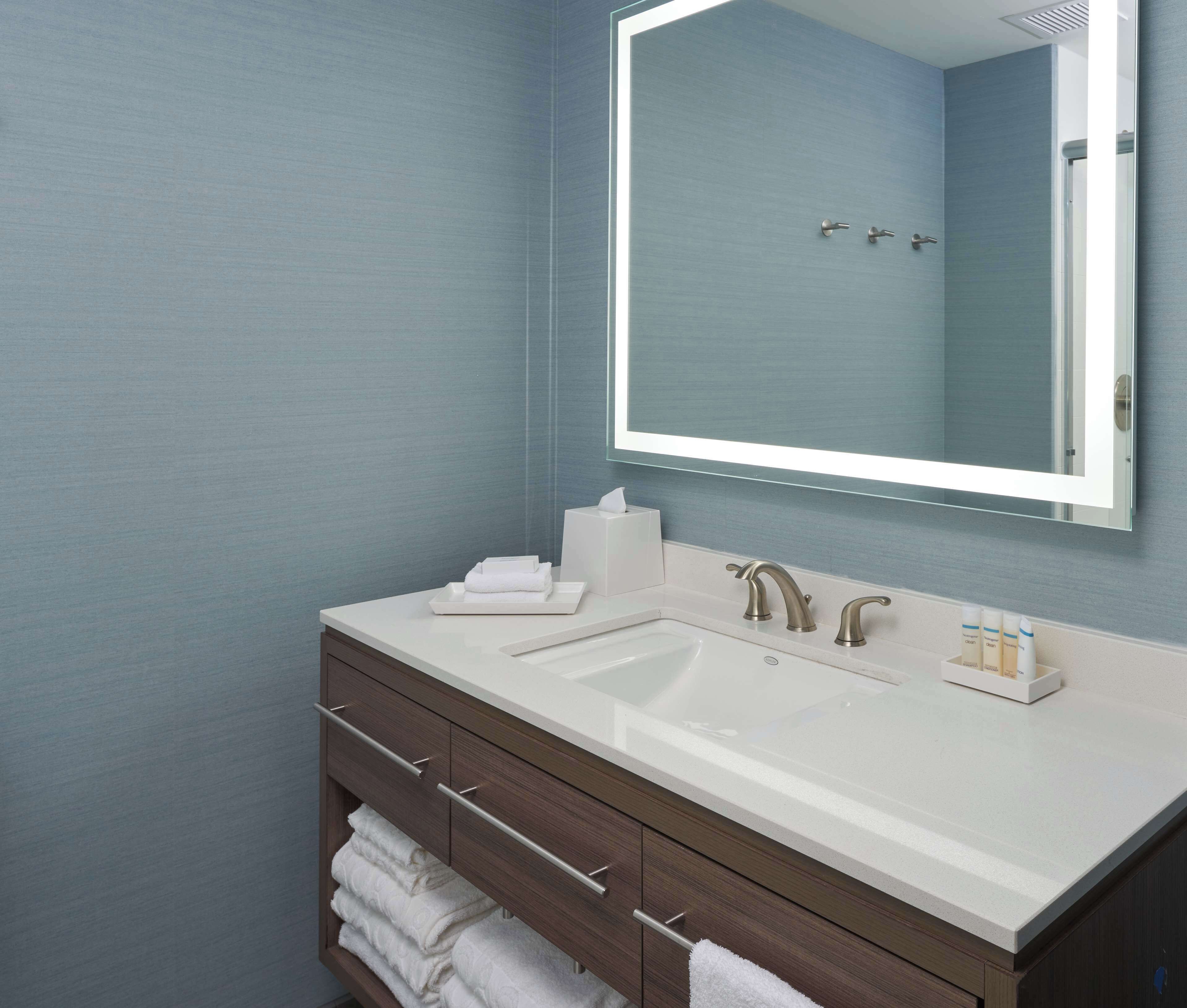 A bathroom with a white sink, two faucets, a mirror, and a towel rack.