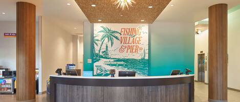 A reception desk with a wooden finish, a sign reading "FISHING VILLAGE & PIER", and a modern ceiling design.