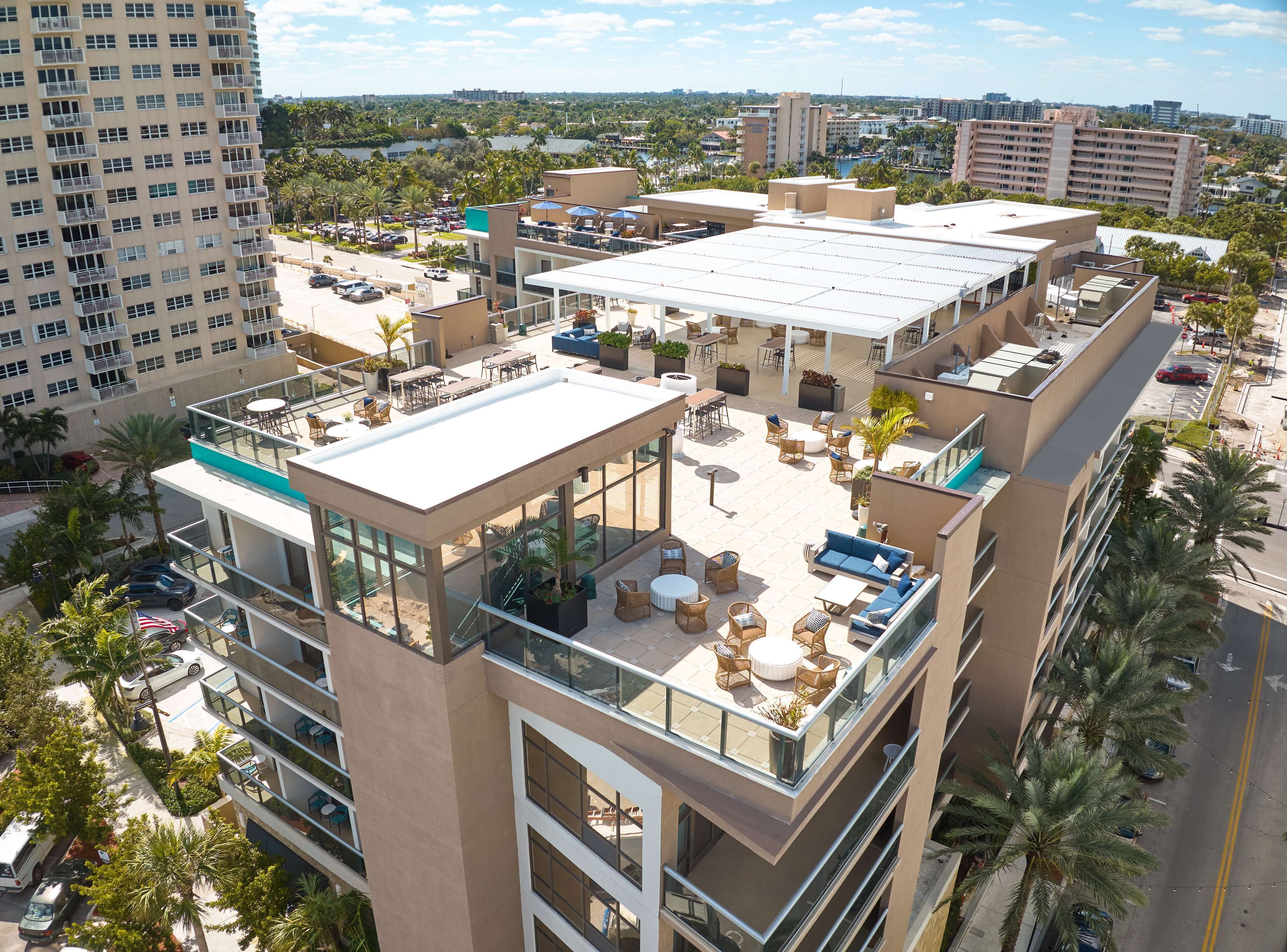 A multi-story hotel with outdoor seating areas, a pool, and a view of the surrounding cityscape.