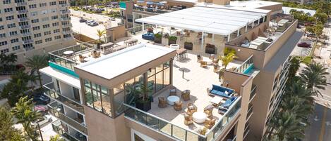 A multi-story hotel with outdoor seating areas, a pool, and a view of the surrounding cityscape.