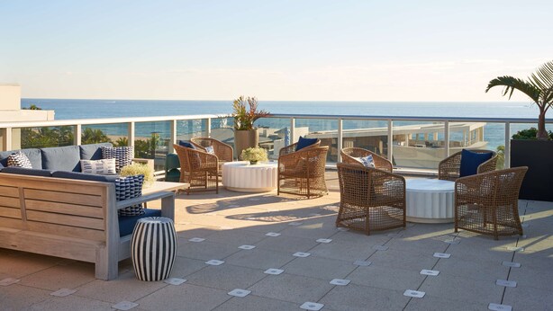 Eine Dachterrasse mit Korbmöbeln, einem runden Tisch und Blick aufs Meer.