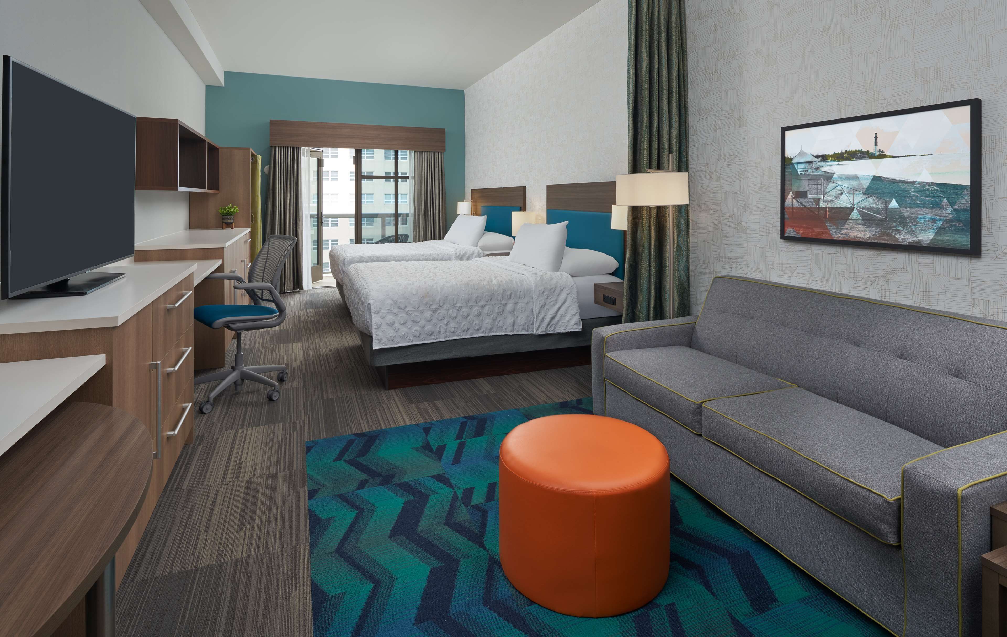 Une chambre d’hôtel avec un lit, un canapé, une télévision, un bureau et un tableau au mur.