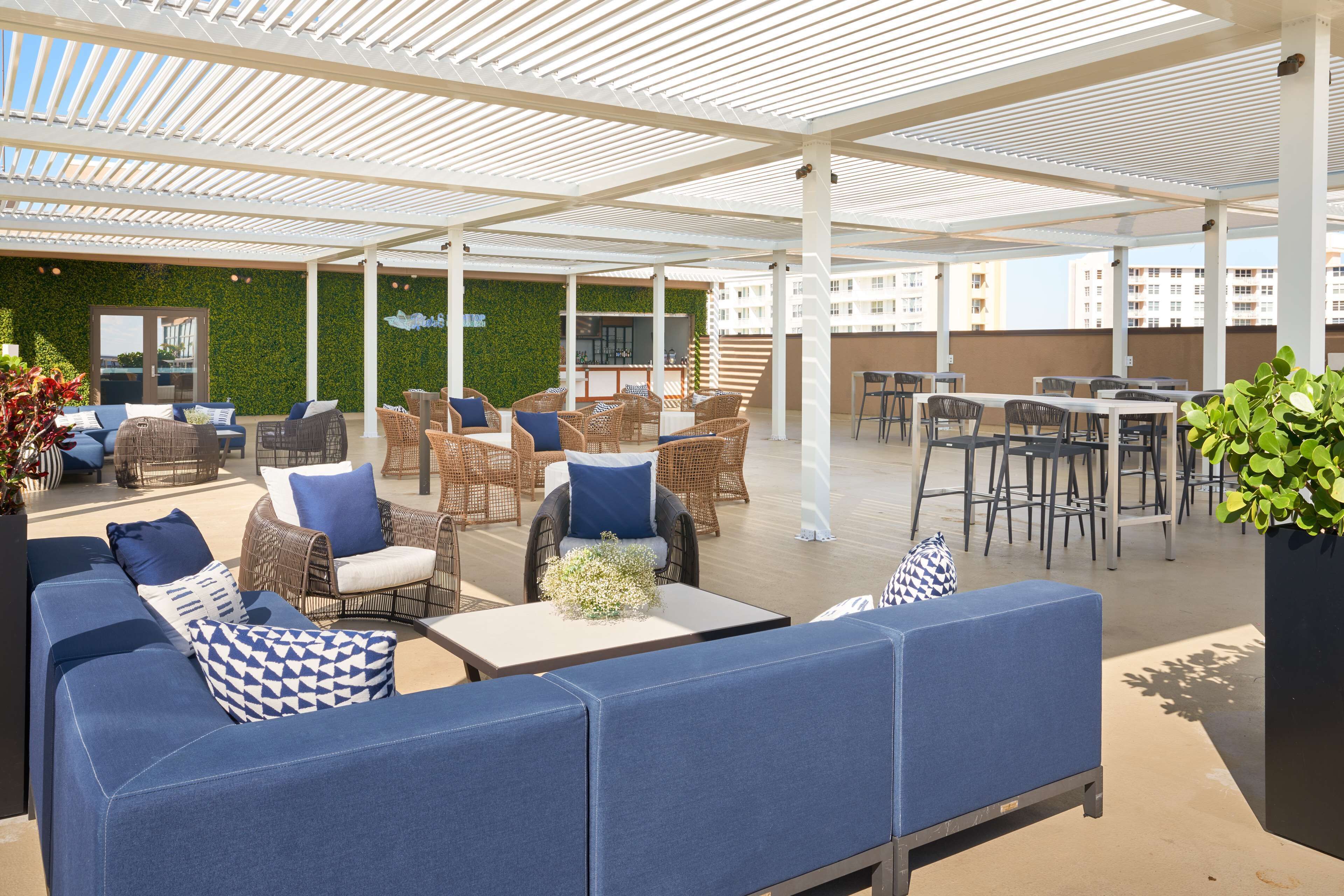 An outdoor patio area with seating arrangements, a bar, and a green wall.