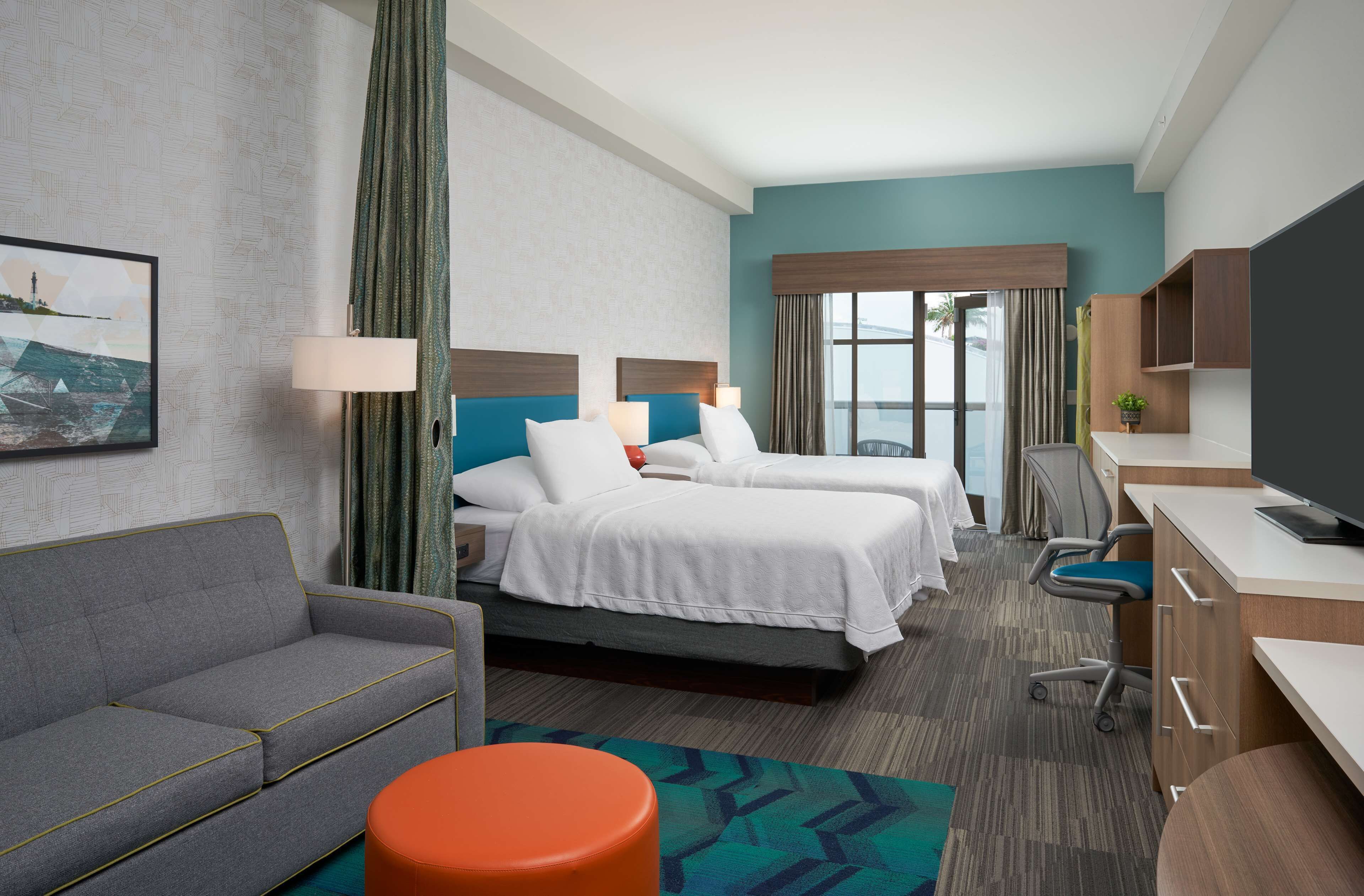 Ein Hotelzimmer mit zwei Betten, einem Sofa, einem Schreibtisch und einem Fernseher.