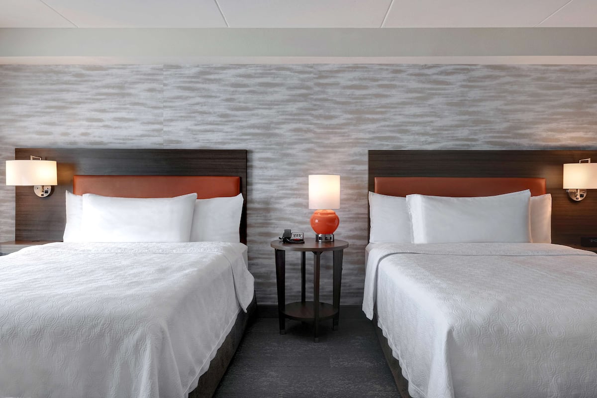 Ett hotellrum med två sängar, ett runt bord med en lampa och en vägg med en intressant yta.