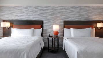Habitación de hotel con dos camas, una mesa redonda con lámpara y pared con textura.