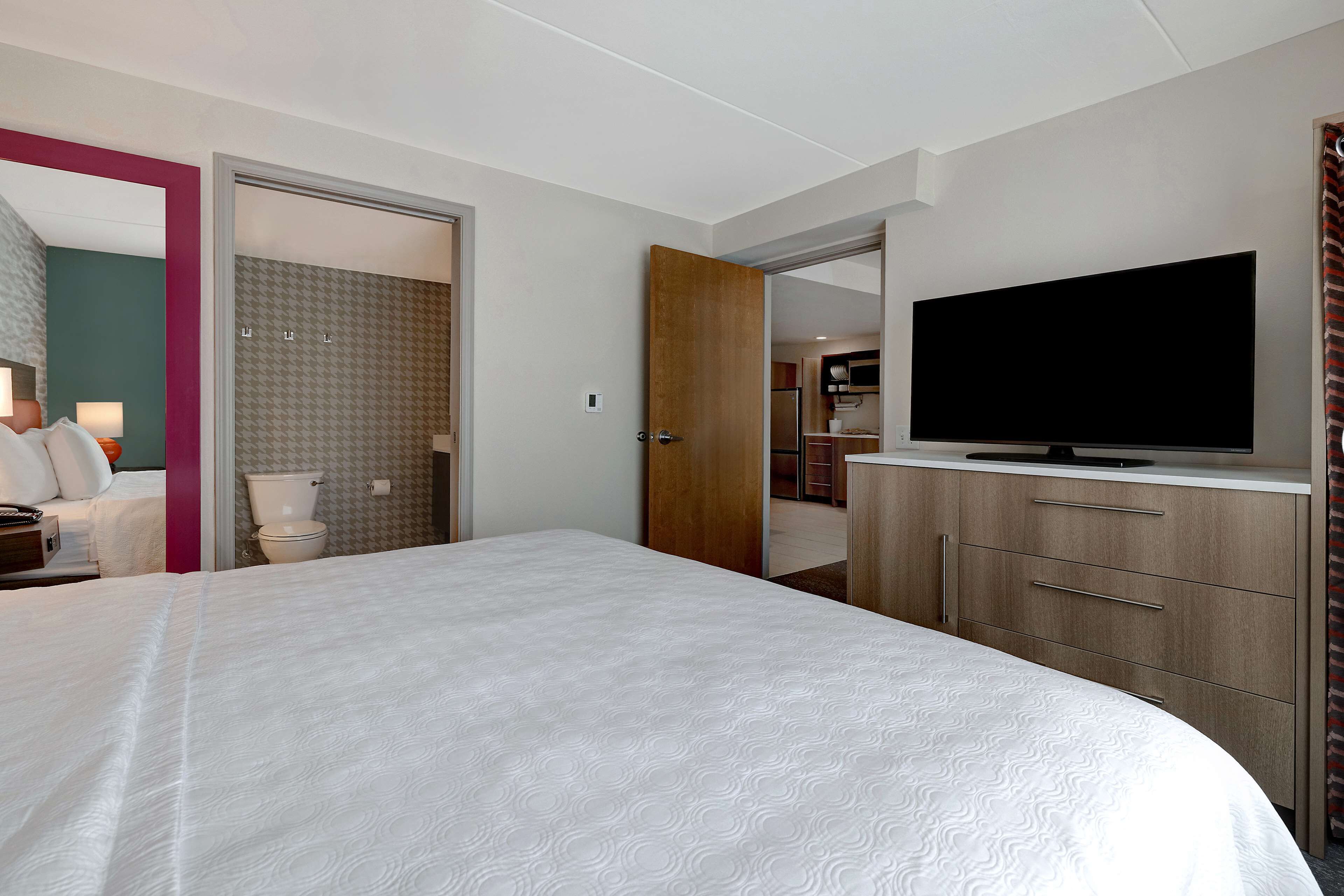 A hotel room with a large bed, a television on a wooden cabinet, and a bathroom visible through an open door.