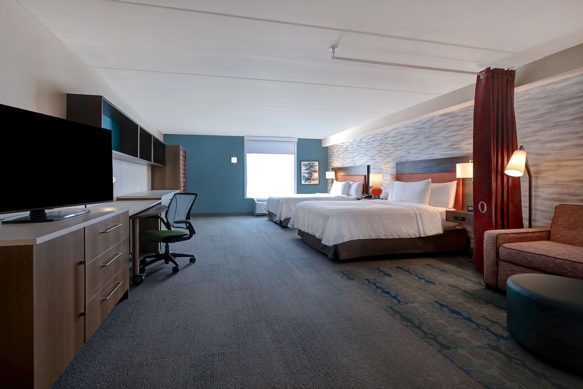 Ett hotellrum med ett skrivbord, två sängar, en TV och en soffa.