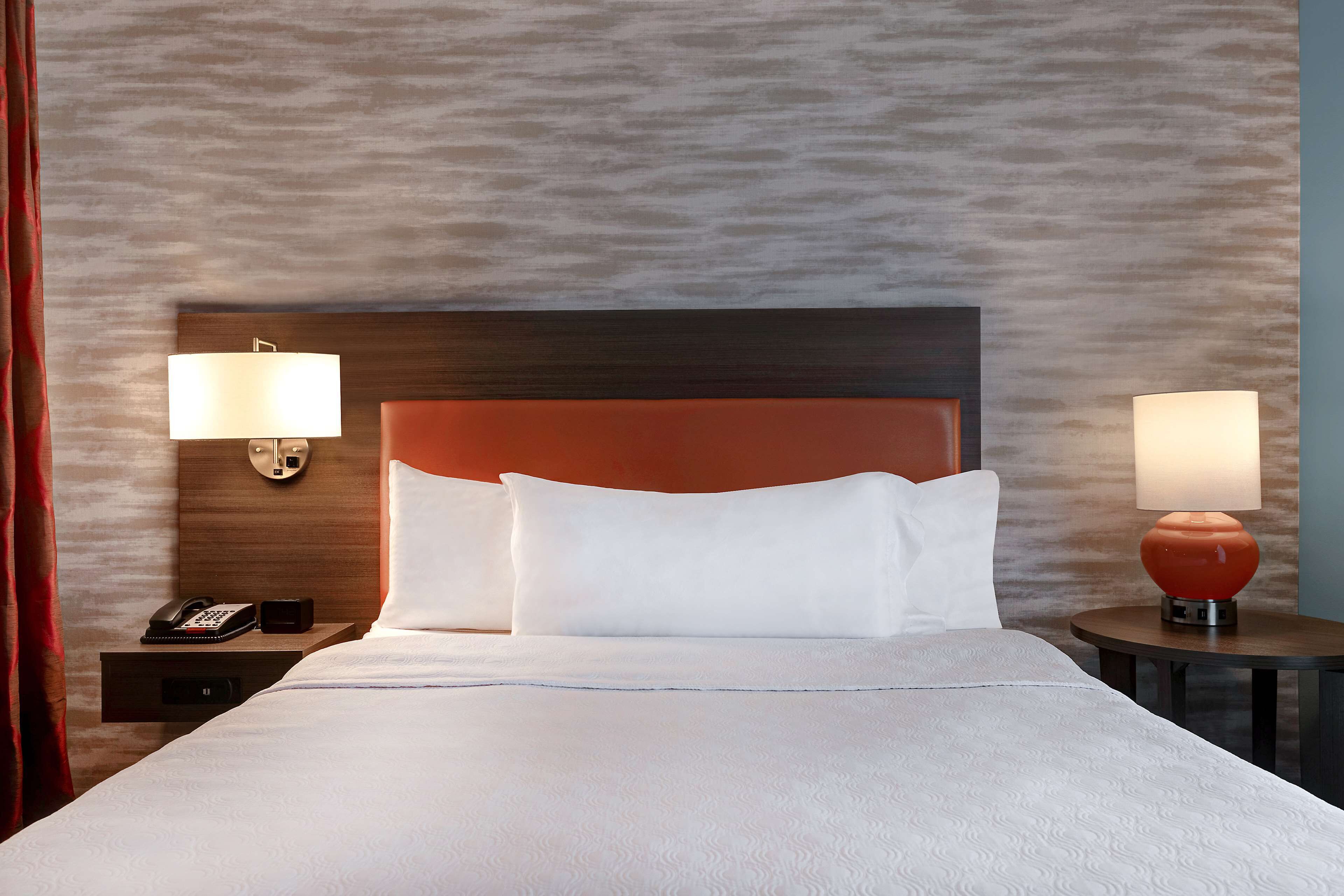 Une chambre d’hôtel avec un grand lit, deux lampes de chevet, une table de chevet avec un téléphone et un mur à motifs.