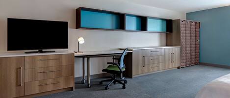 A hotel room with a bed, a desk with a chair, a television, and a wardrobe.