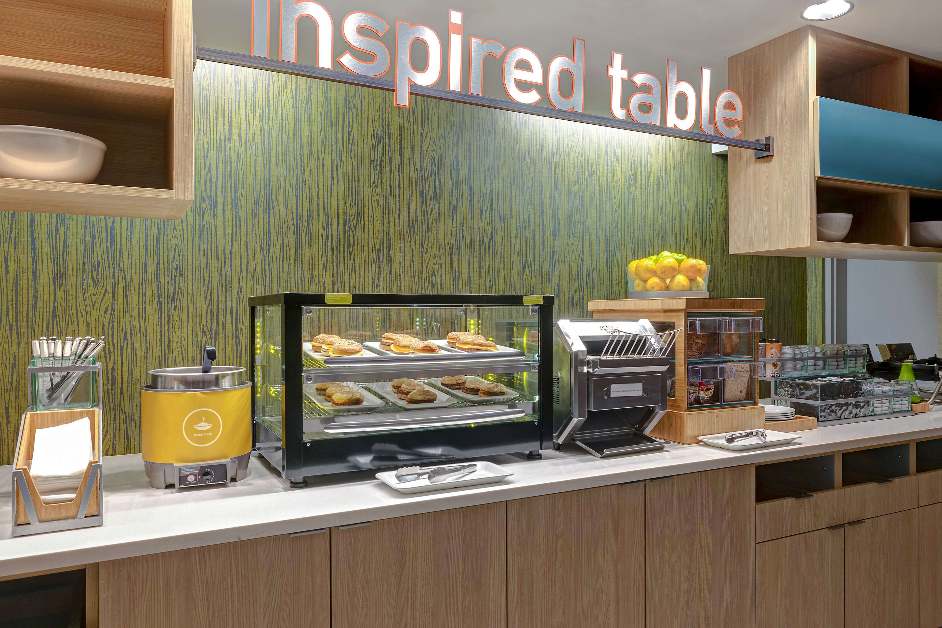 A breakfast bar with a display case of pastries, a coffee machine, and a sign reading "Inspired Table".
