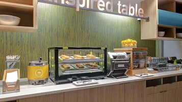 A breakfast bar with a display case of pastries, a coffee machine, and a sign reading "Inspired Table".