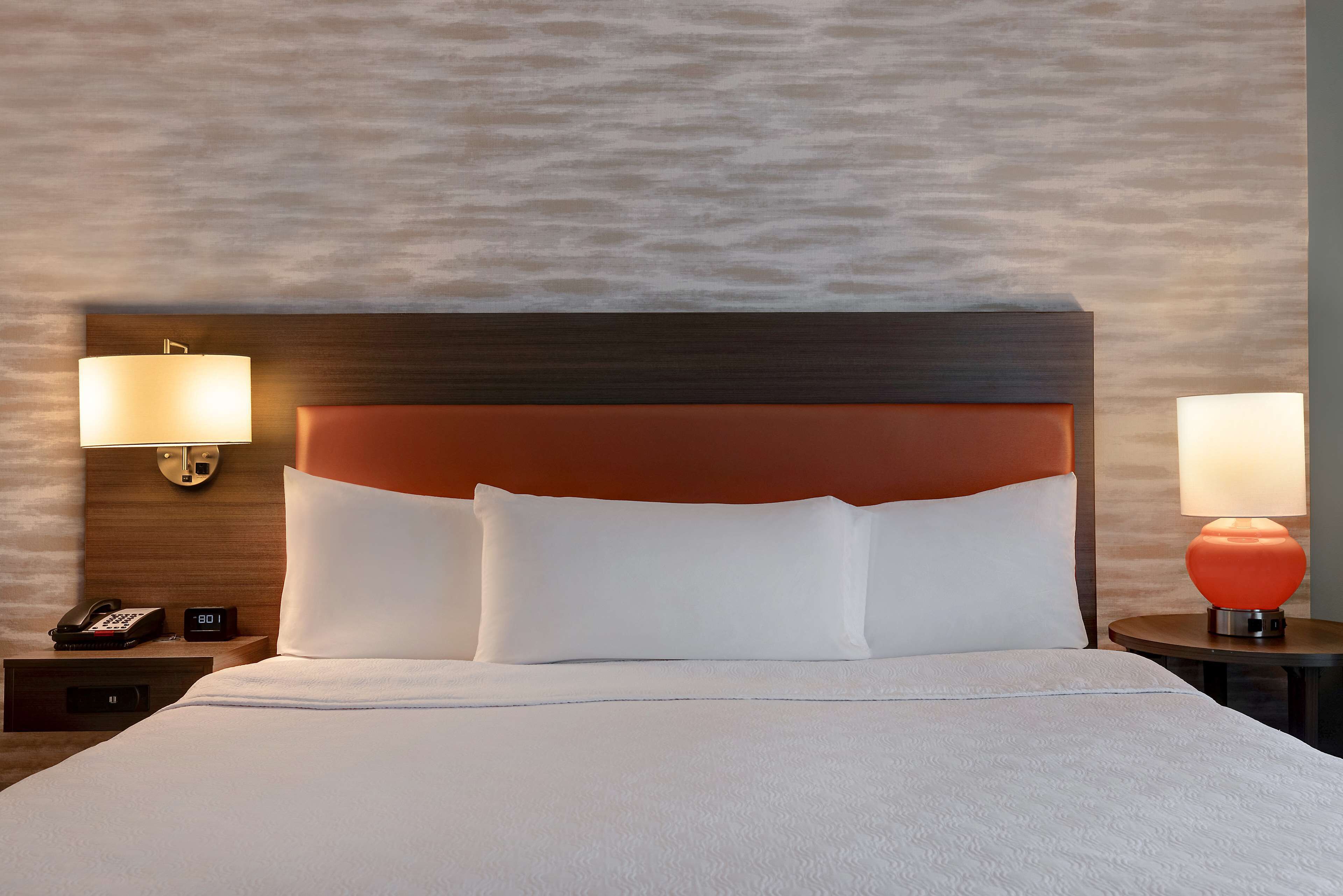 A hotel room with a large bed, two bedside lamps, a nightstand with a phone, and a wall-mounted lamp.
