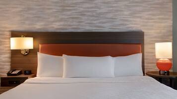 Quarto de hotel com uma cama grande, duas luminárias de cabeceira, uma mesa de cabeceira com telefone e uma luminária na parede.