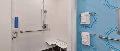 Une salle de bain équipée d’une douche, de barres d’appui, d’un banc blanc et d’un mur bleu orné d’un motif à pois.