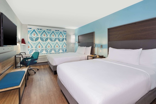 A hotel room with two beds, a desk with a chair, a TV, and a patterned wall.