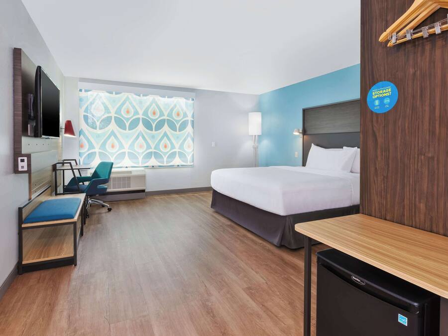 A hotel room with a bed, a desk, a chair, a TV, and a mini fridge.