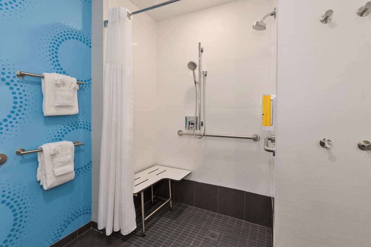 A modern bathroom with a shower, grab bars, and a white towel rack.