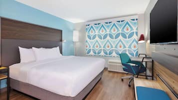 Habitación de hotel con una cama grande, un escritorio con silla, un televisor y un papel tapiz estampado.