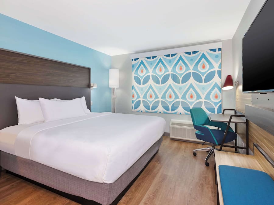 Habitación de hotel con una cama grande, un escritorio con silla, un televisor y un papel tapiz estampado.