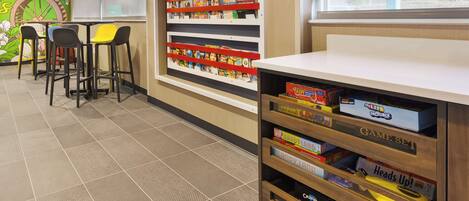 A children's play area with a mural, a bookshelf with games, and a seating area with chairs.