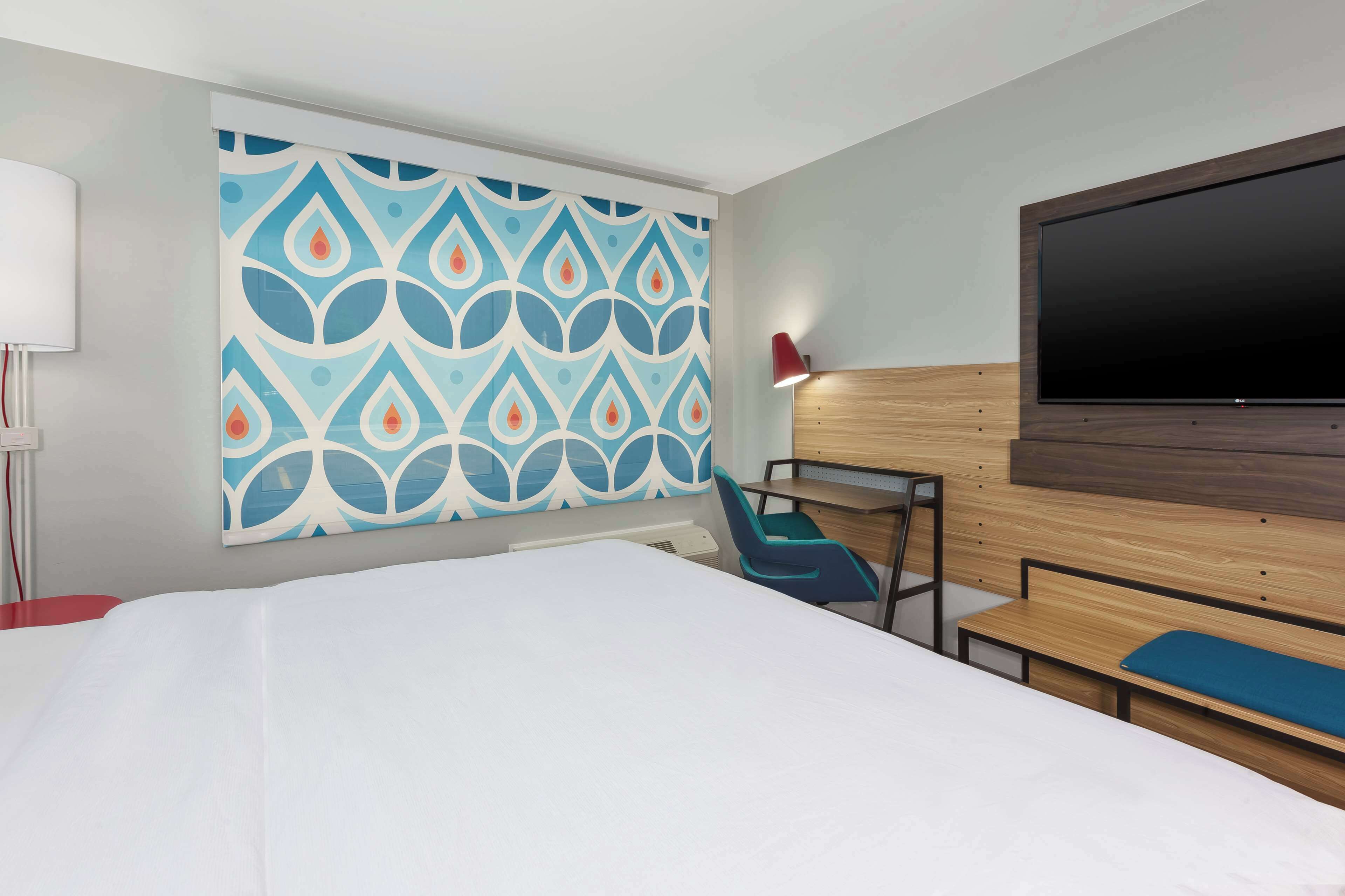 Une chambre d’hôtel avec un grand lit, un téléviseur fixé au mur, un mur décoré d’un motif, un bureau et une chaise.