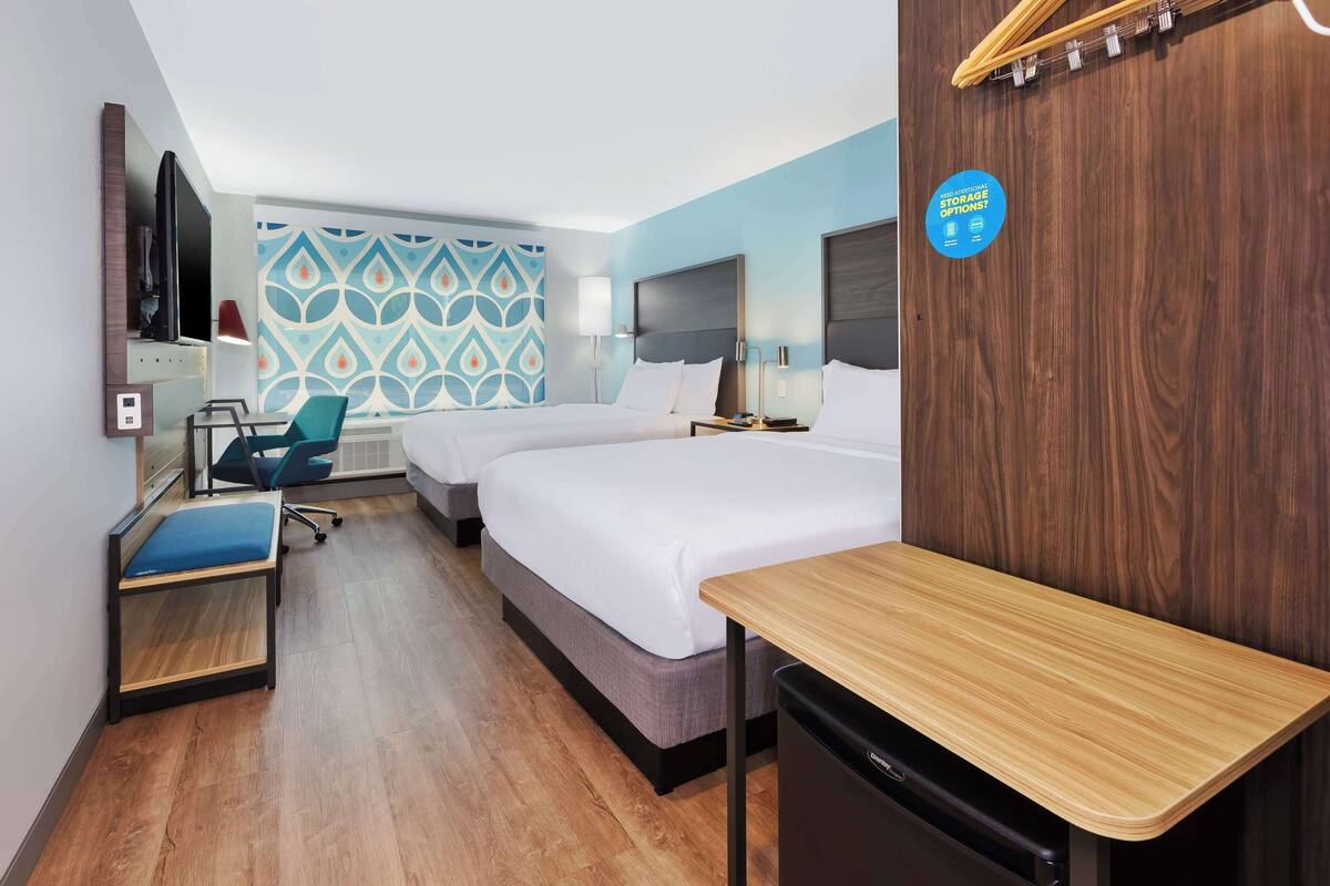 A hotel room with two beds, a desk, a chair, a TV, and a wall with a storage sign.